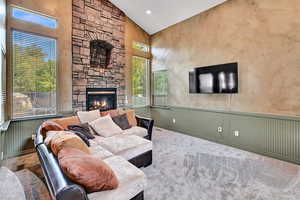 Carpeted living room featuring high vaulted ceiling and a stone fireplace