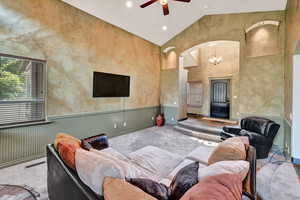 Living room with ceiling fan with notable chandelier, light colored carpet, and high vaulted ceiling