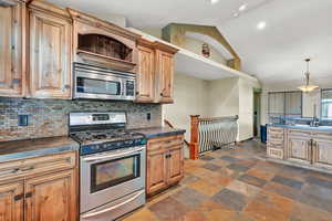 Kitchen featuring high vaulted ceiling, sink, decorative backsplash, appliances with stainless steel finishes, and decorative light fixtures