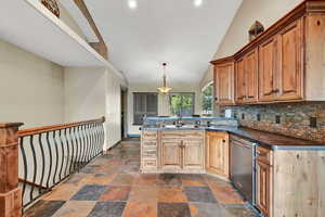 Kitchen with dishwasher, sink, hanging light fixtures, lofted ceiling, and decorative backsplash