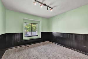 Carpeted empty room featuring a textured ceiling and track lighting