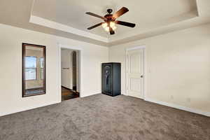 Unfurnished bedroom with a raised ceiling, a walk in closet, ceiling fan, and dark colored carpet