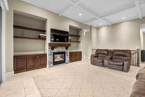 Living room with built in shelves, a stone fireplace, beamed ceiling, and coffered ceiling