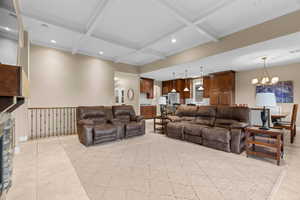 Tiled living room featuring beamed ceiling, an inviting chandelier, coffered ceiling, and a stone fireplace