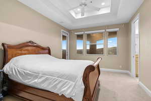 Bedroom featuring ceiling fan, light colored carpet, and a tray ceiling