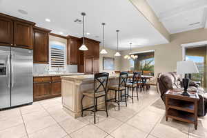 Kitchen featuring a kitchen bar, light stone counters, decorative light fixtures, stainless steel fridge with ice dispenser, and a center island