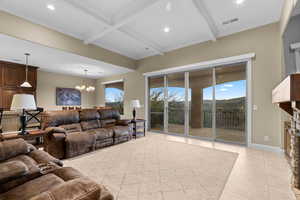 Tiled living room with coffered ceiling, a stone fireplace, beamed ceiling, a chandelier, and ornamental molding