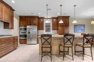 Kitchen featuring pendant lighting, a center island, backsplash, a kitchen breakfast bar, and appliances with stainless steel finishes