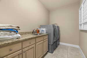 Clothes washing area with cabinets, washing machine and dryer, light tile patterned floors, and sink