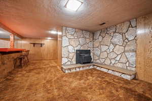 Unfurnished living room with a wood stove, a textured ceiling, indoor bar, wooden walls, and carpet