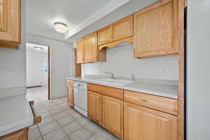 Kitchen featuring light tile patterned flooring, light brown cabinets, white dishwasher, and sink