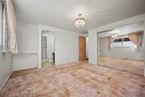 Unfurnished bedroom with ensuite bath, a closet, carpet, and a notable chandelier