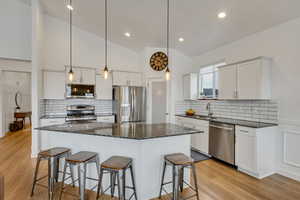 Kitchen featuring white cabinets, hanging light fixtures, tasteful backsplash, a kitchen island, and stainless steel appliances