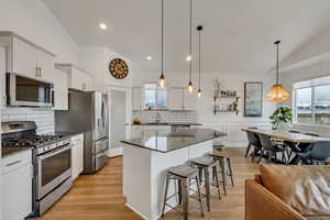 Kitchen with stainless steel appliances, vaulted ceiling, white cabinets, a kitchen island, and hanging light fixtures