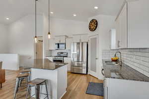 Kitchen with pendant lighting, dark stone counters, white cabinets, sink, and stainless steel appliances