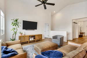 Living room with hardwood / wood-style floors, ceiling fan, and high vaulted ceiling