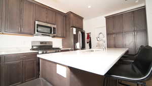 Kitchen featuring a breakfast bar, sink, dark brown cabinets, and appliances with stainless steel finishes