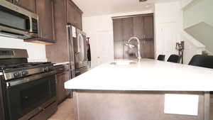 Kitchen featuring sink, a kitchen breakfast bar, an island with sink, dark brown cabinets, and appliances with stainless steel finishes