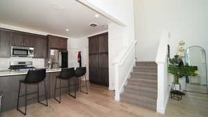 Kitchen featuring appliances with stainless steel finishes, light wood-type flooring, dark brown cabinetry, and a breakfast bar area