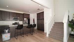 Kitchen with dark brown cabinetry, a center island, a kitchen breakfast bar, appliances with stainless steel finishes, and light wood-type flooring