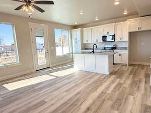 Kitchen with light stone countertops, light hardwood / wood-style flooring, a center island with sink, white cabinets, and appliances with stainless steel finishes