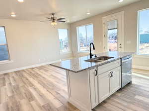 Kitchen with light stone countertops, stainless steel dishwasher, sink, a center island with sink, and white cabinetry