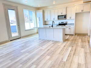 Kitchen featuring white cabinetry, light stone counters, white range oven, a kitchen island with sink, and light wood-type flooring