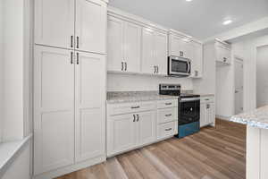 Kitchen with stainless steel appliances, light wood-type flooring, white cabinets, light stone countertops, and recessed lighting