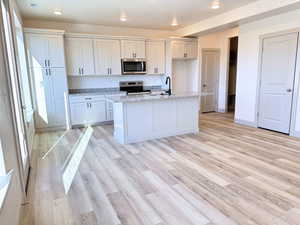 Kitchen with light stone countertops, white cabinetry, an island with sink, and appliances with stainless steel finishes