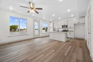 Kitchen with an island with sink, white cabinetry, light wood-type flooring, electric stove, and open floor plan