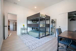 Bedroom with light wood-type flooring, stainless steel refrigerator, and a closet