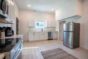 Kitchen with white cabinets, appliances with stainless steel finishes, light wood-type flooring, and sink