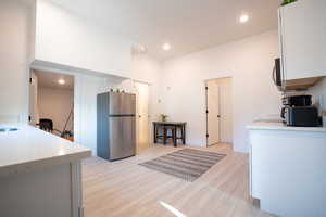 Kitchen with stainless steel fridge, light wood-type flooring, white cabinetry, and sink