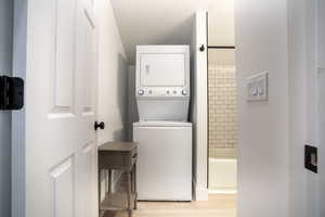 Washroom with light hardwood / wood-style floors, stacked washing maching and dryer, and a textured ceiling