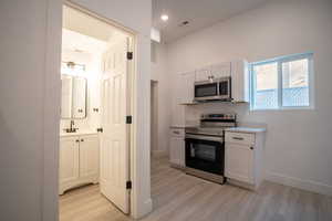 Kitchen with light wood-type flooring, stainless steel appliances, and white cabinetry