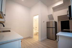 Kitchen with stainless steel fridge, white cabinetry, sink, and light hardwood / wood-style flooring