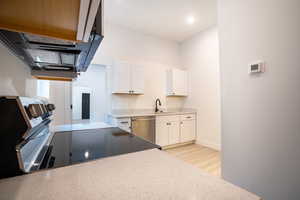 Kitchen with stainless steel appliances, white cabinetry, light hardwood / wood-style floors, and sink