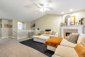 Living room with ceiling fan, vaulted ceiling, light colored carpet, and a tiled fireplace