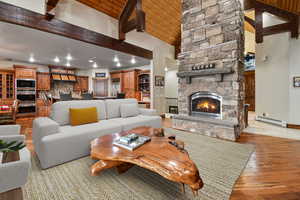 VIRTUALLY STAGED - Living room featuring a baseboard radiator, a stone fireplace, beamed ceiling, high vaulted ceiling, and light hardwood / wood-style floors