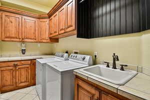 Washroom featuring washing machine and dryer, sink, light tile patterned floors, and cabinets