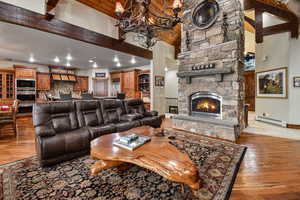 Living room with beam ceilingan inviting chandelier, light hardwood / wood-style floors, and a stone fireplace