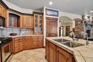 Kitchen with tile countertops, a stone fireplace, sink, gas range, and light tile patterned floors