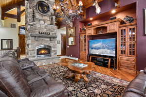 Living room featuring hardwood / wood-style floors, a stone fireplace, beam ceiling, and wood ceiling