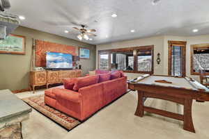 Carpeted living room with ceiling fan and pool table