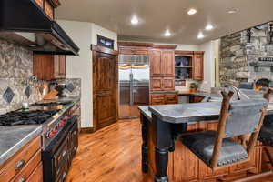 Kitchen with decorative backsplash, light wood-type flooring, sink, stainless steel built in fridge, and a breakfast bar area