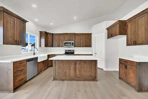 Kitchen featuring vaulted ceiling, a kitchen island, appliances with stainless steel finishes, sink, and light hardwood / wood-style floors