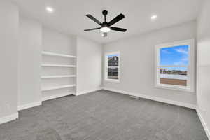 Unfurnished room with built in shelves, carpet floors, and ceiling fan