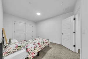 Carpeted bedroom with baseboards, visible vents, and a closet