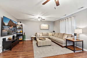 Living room with a textured ceiling, ceiling fan, and dark wood-type flooring