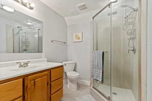 Basement bathroom featuring walk in shower, tile patterned floors, vaulted ceiling, toilet, and vanity